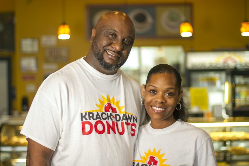 Male and female owners of Krack of Dawn Donuts stand in their bakery.